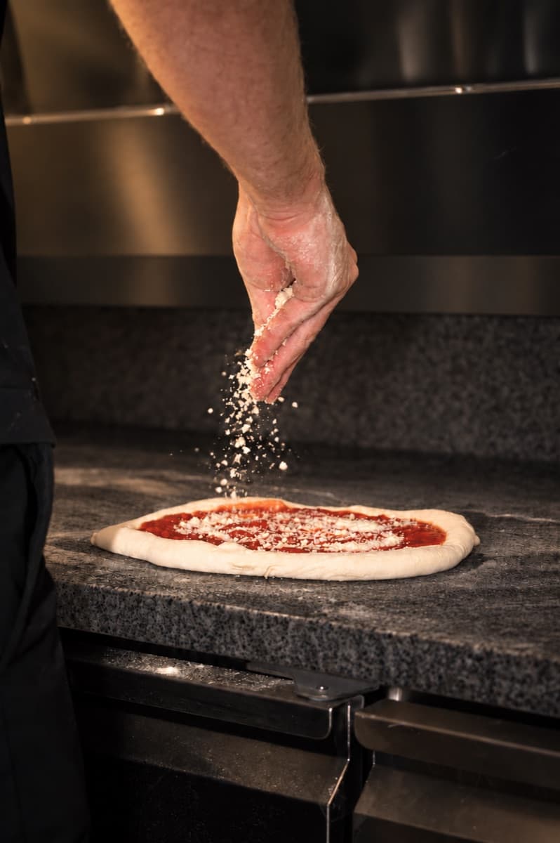 A hand sprinkling grated cheese over a tomato base