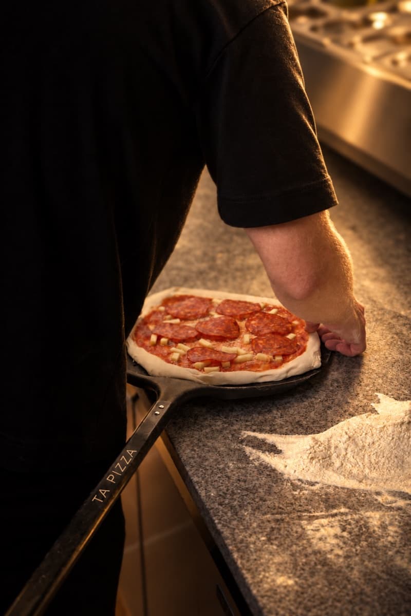 A raw salami pizza on a peel branded TA PIZZA